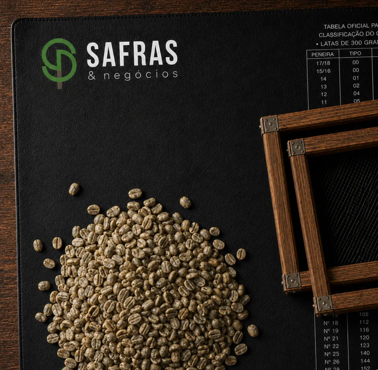 Grãos de café verde sobre tapete preto Safras & Negócios, ao lado de peneira de classificação