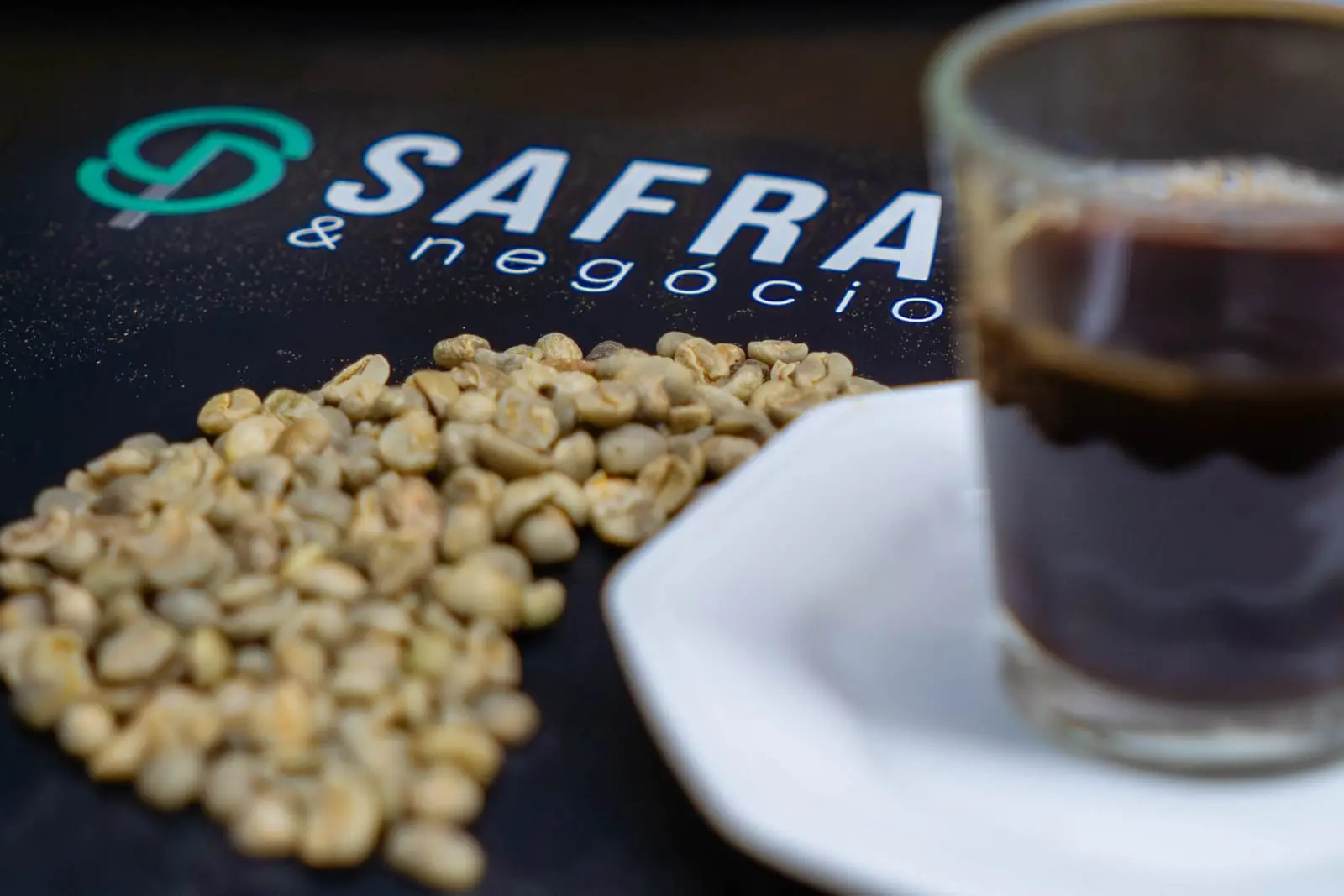 Grãos de café verde e xícara de café sobre o tapete da Safras & Negócios